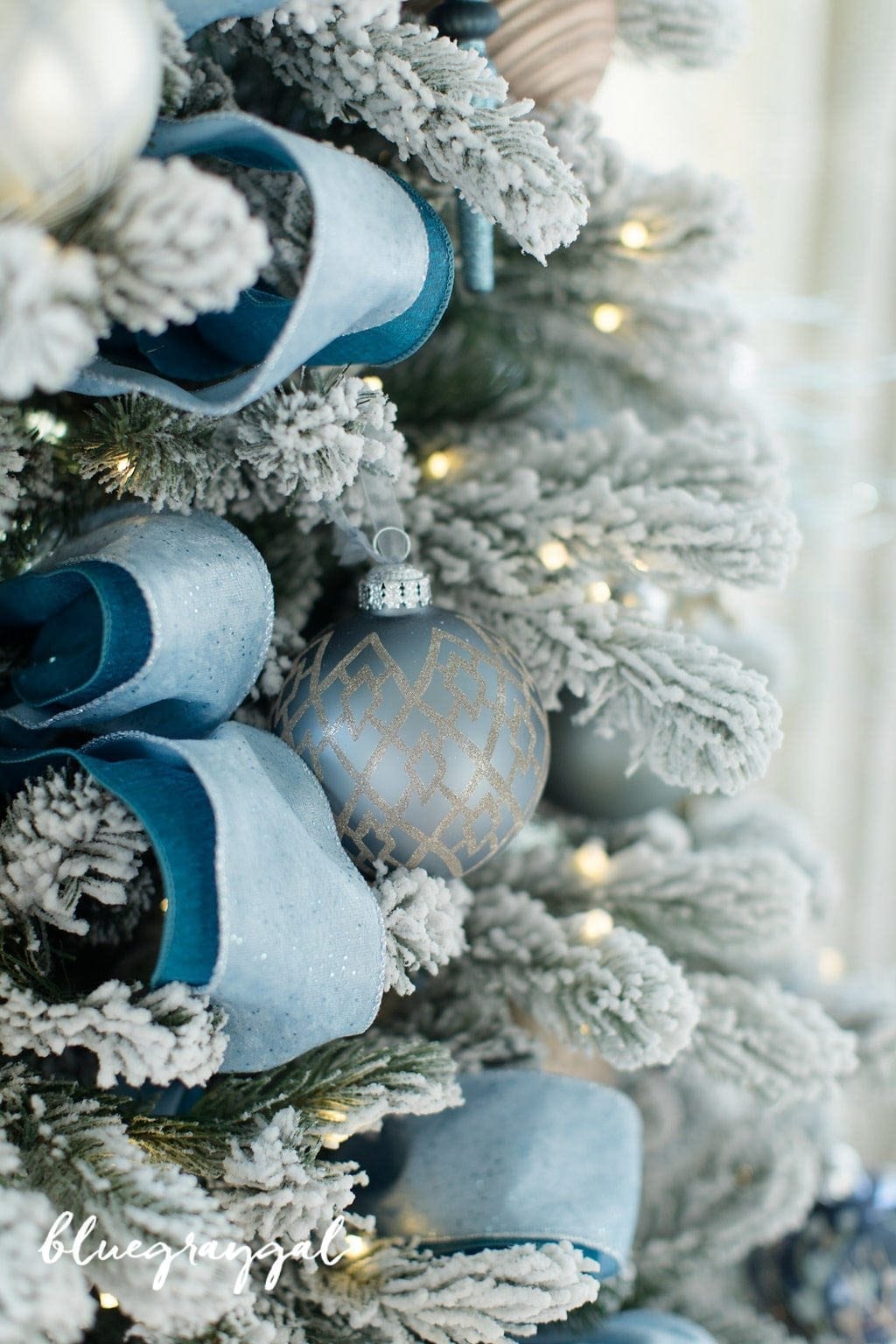 peacock blue ribbon on a pre lit artificial flocked tree with blue and gray ornaments