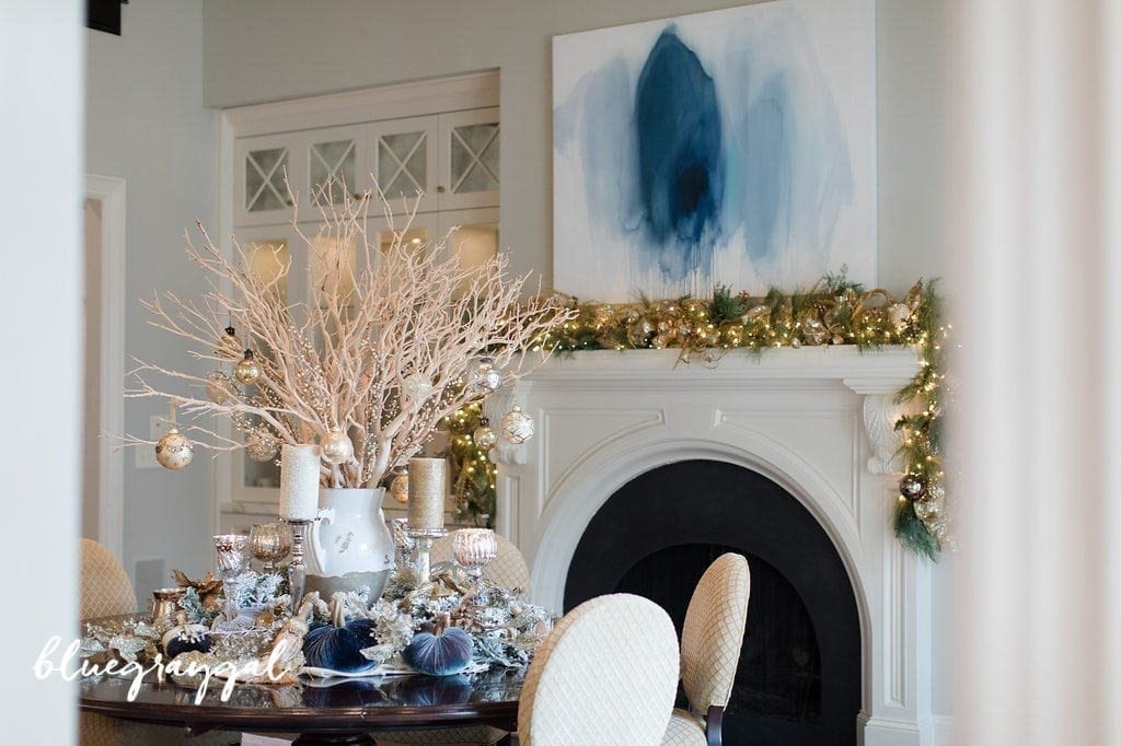 Manzanita branches with christmas ornaments and flocked garland around it in a dining room with blue wall art. How to decorate a table for Thanksgiving. Creating a manzanita centerpiece for a table.