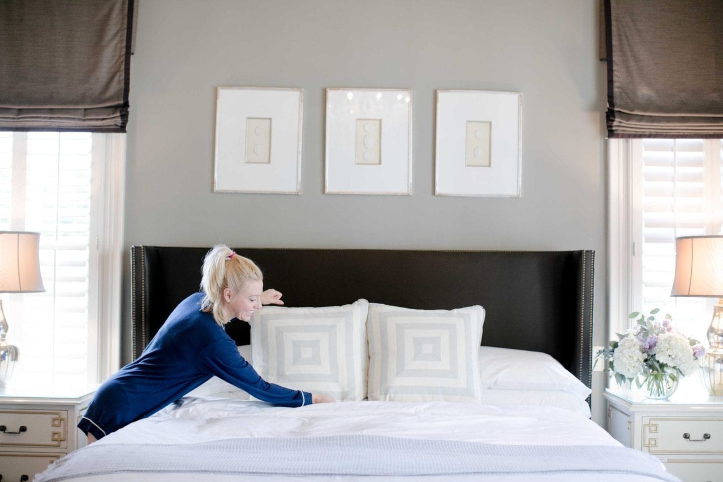 blonde girl in blue soft pajamas making a bed with blue and white square pillows