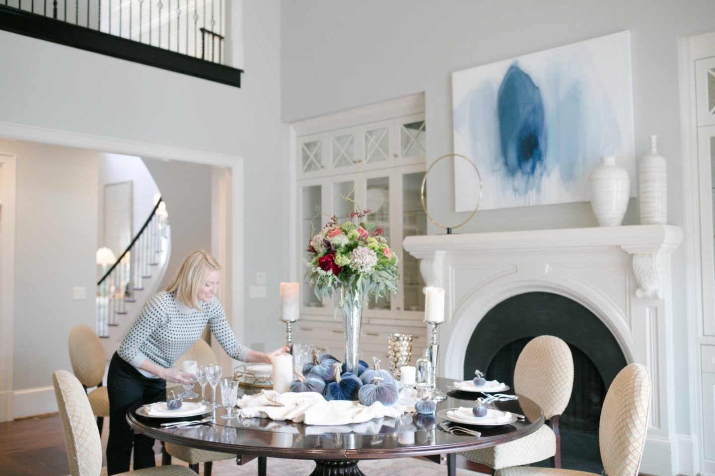 Round dining room table setting with tall floral arrangement.