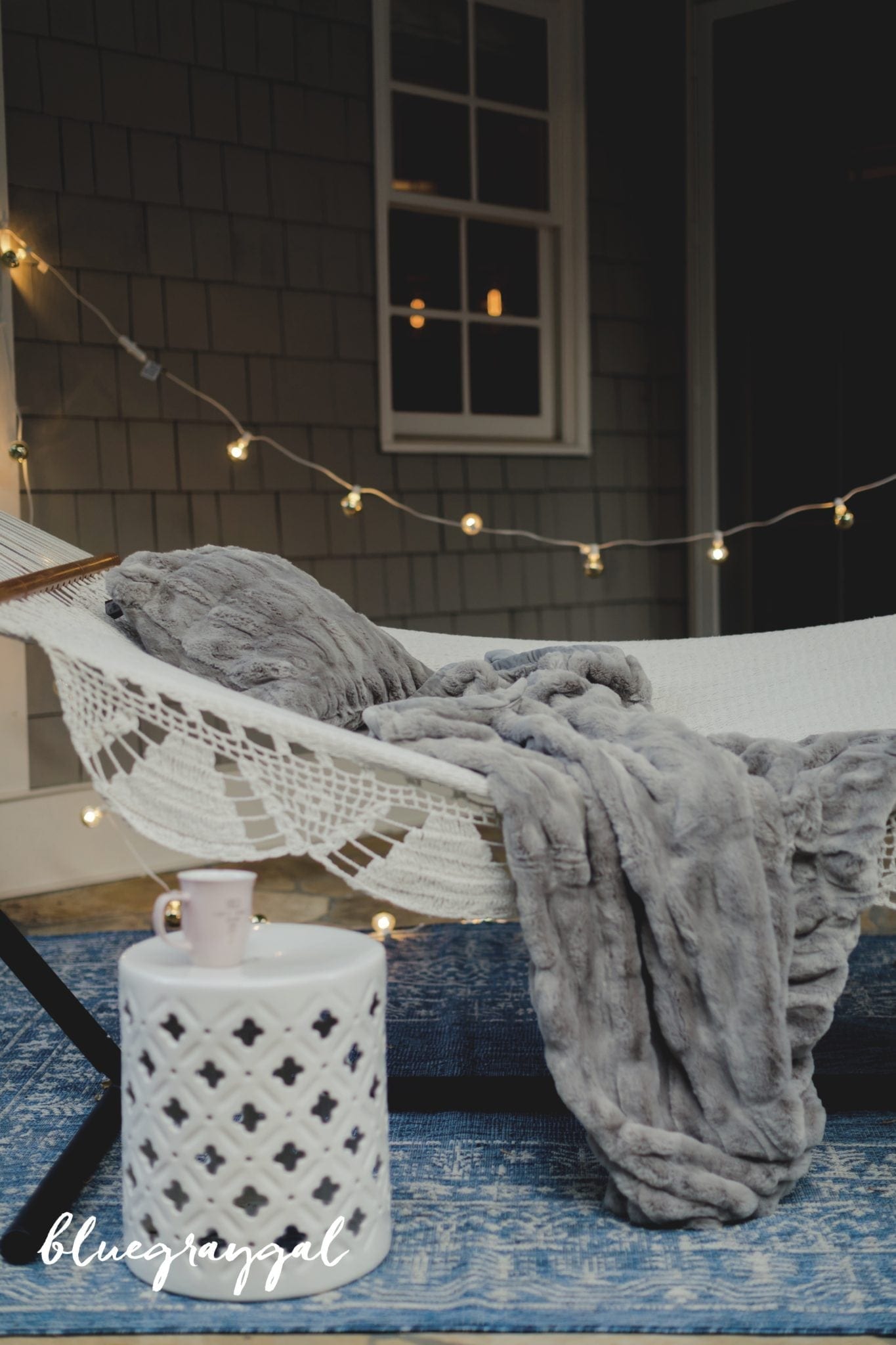 winter hammock hanging outside with white garden stool and winter lights and faur fur gray blanket