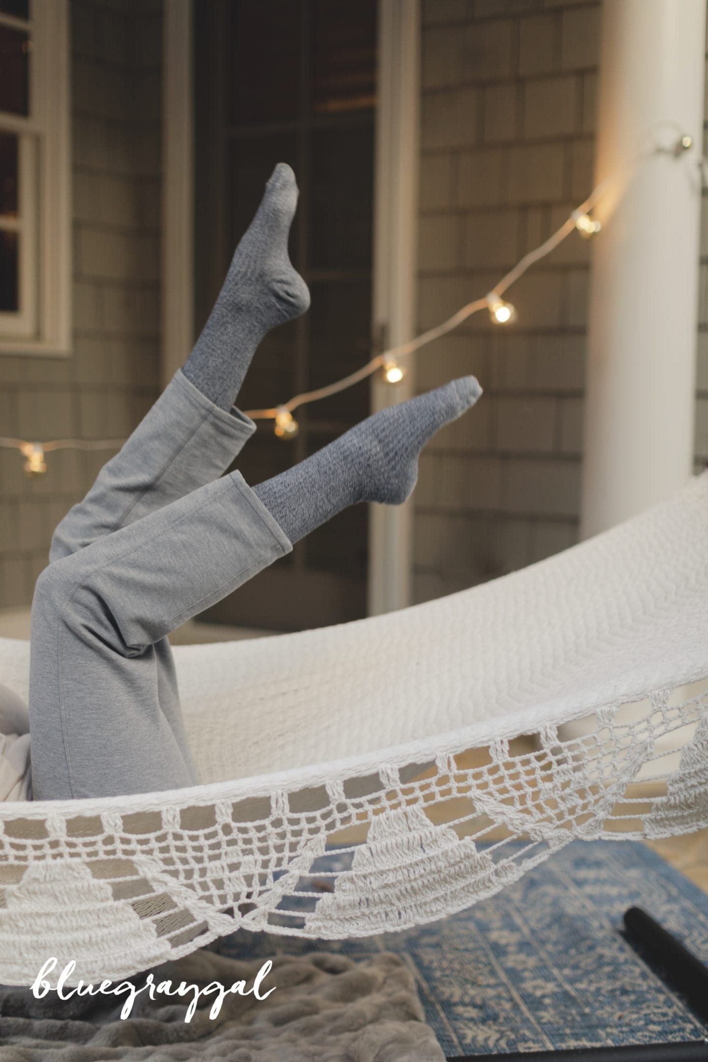 outdoor hammock hanging by house with gray cedar shingles and cafe lights with girl in gray socks and gray pants