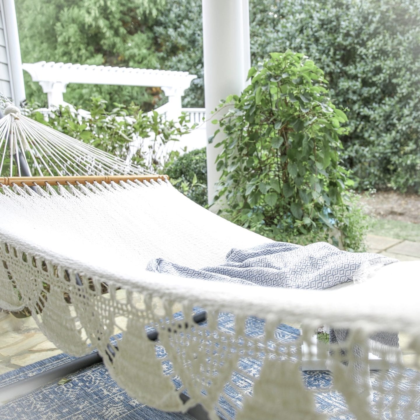 woven hammock outside with indoor outdoor blanket by cape code white gate and climbing hydrangea bush