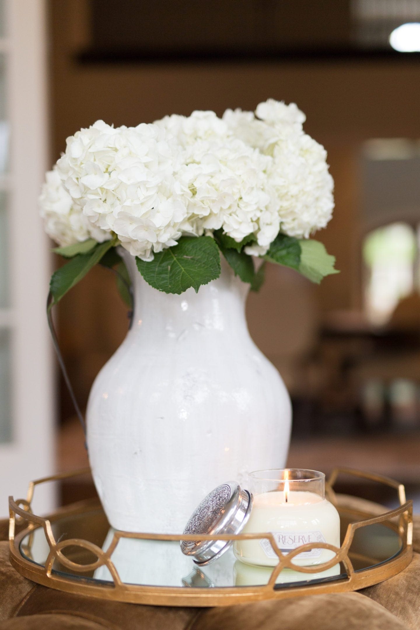 aspen bay reserve candles White hydrangeas in white urn set the stage for a welcoming and soothing living room. A beautiful candle from Aspen Bay Candles is so lovely in white with an etched silver top that it looks just as pretty closed as it does lit and it's a very strong smelling candle! Gold crushed velvet bottom in neutral decor living room.