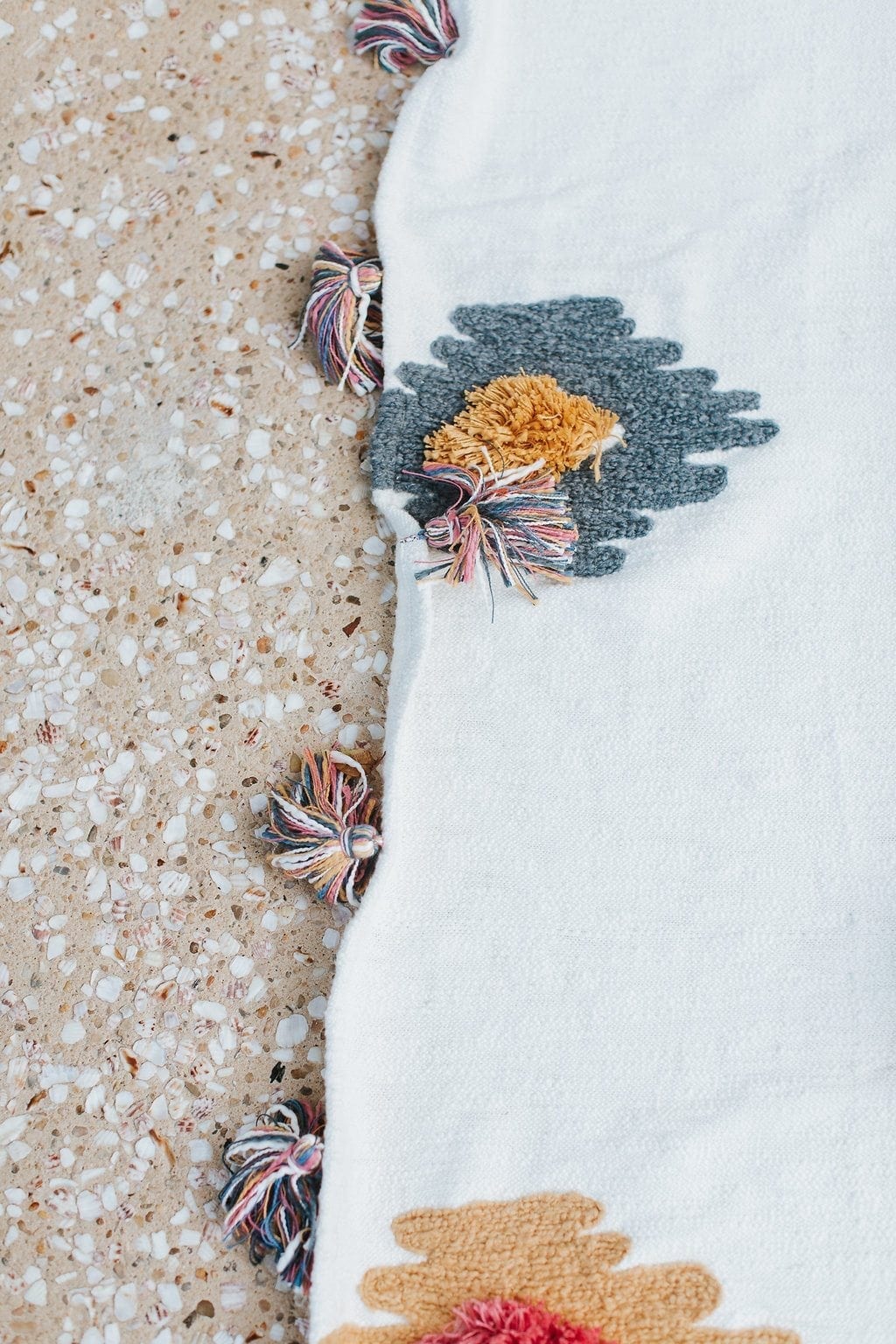An Anthropologie home decor throw blanket is shown with adorable pom poms and tassels and brightly colored floral embroidery.