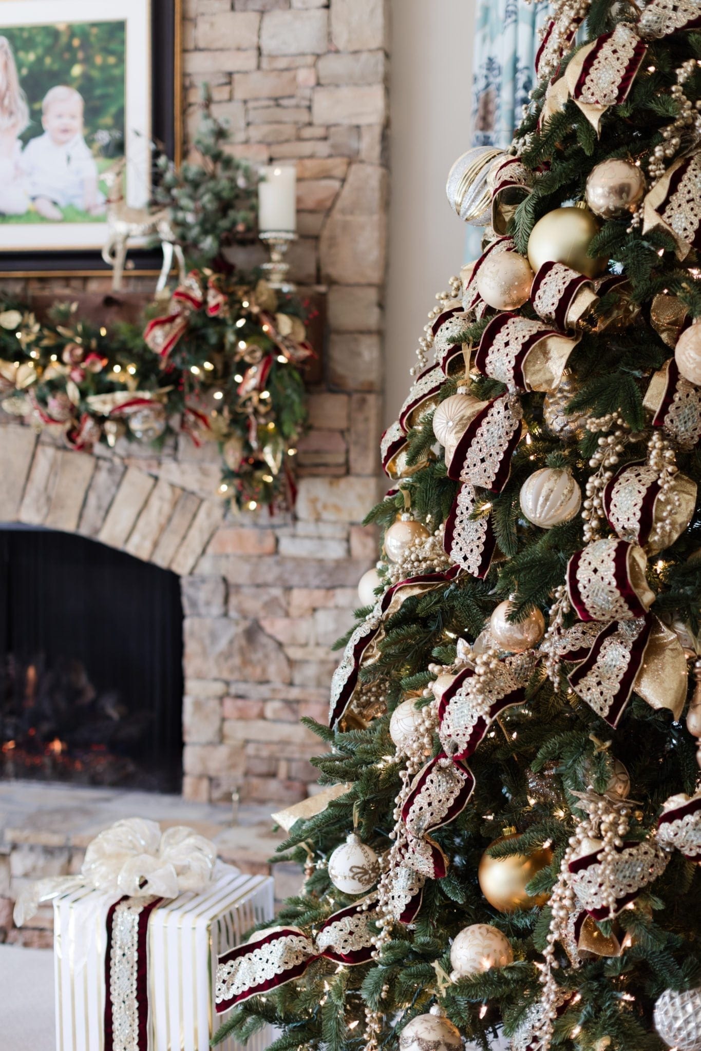 Stone fireplace with Christmas decor on mantle. Frontgate artificial tree with gold and red decorations.