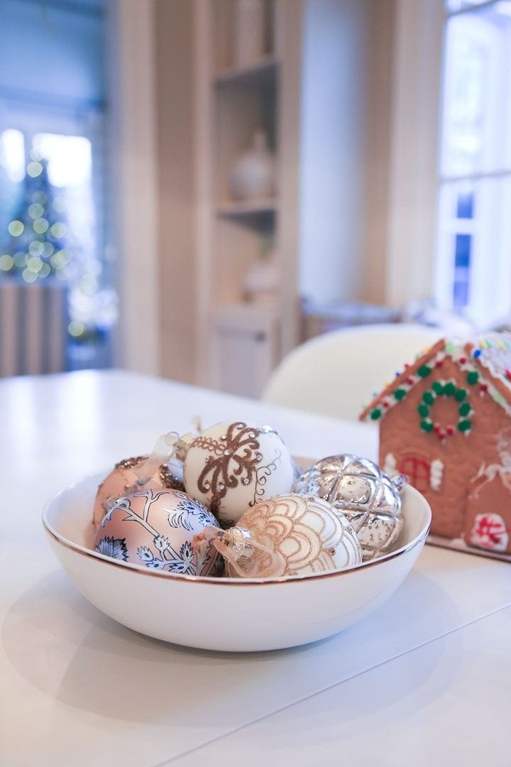 Gold glass ornaments and gingerbread house on kitchen table.