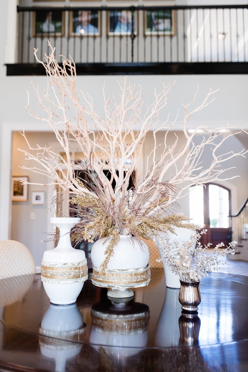 Manzanita Branches used as dining room centerpiece for round dining room table. White urns filled with branches and gold ribbon detail wrapped around urns.