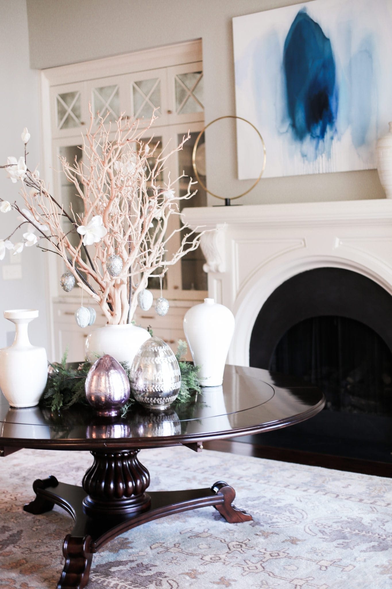 Easter centerpiece on a round dining room table. White urns with manzanita branches and faux magnolia leaves.