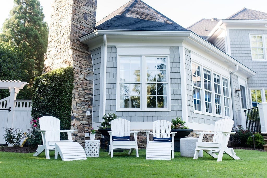 A gray exterior home paint color mixed with a stacked stone fireplace, a white cedar gate and white Adirondack chairs.