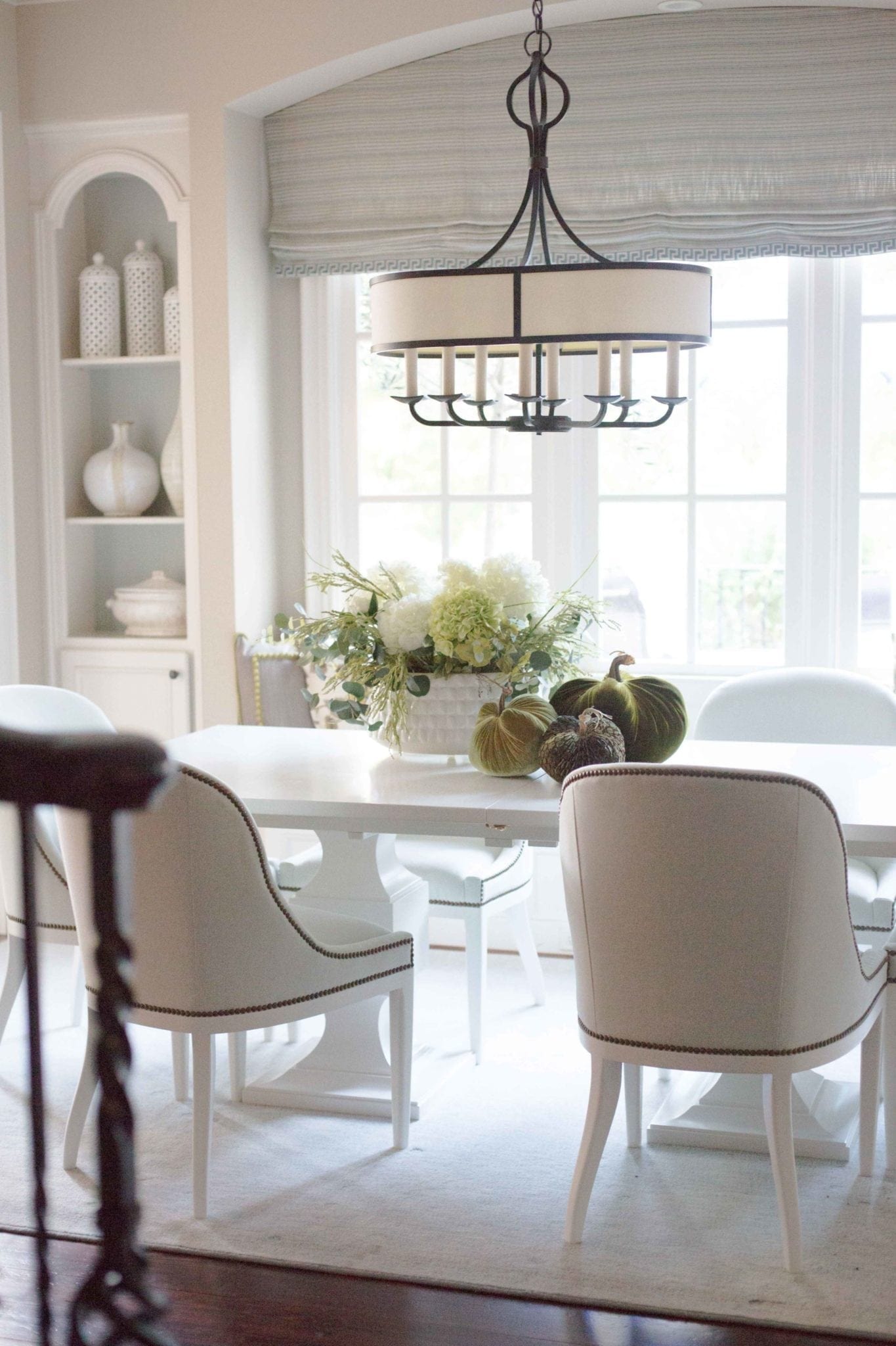 Green velvet pumpkins in white kitchen table. Pretty fall decor. White kitchen table with light blue chairs and white hydrangea arrangement for a soft and pretty fall table!
