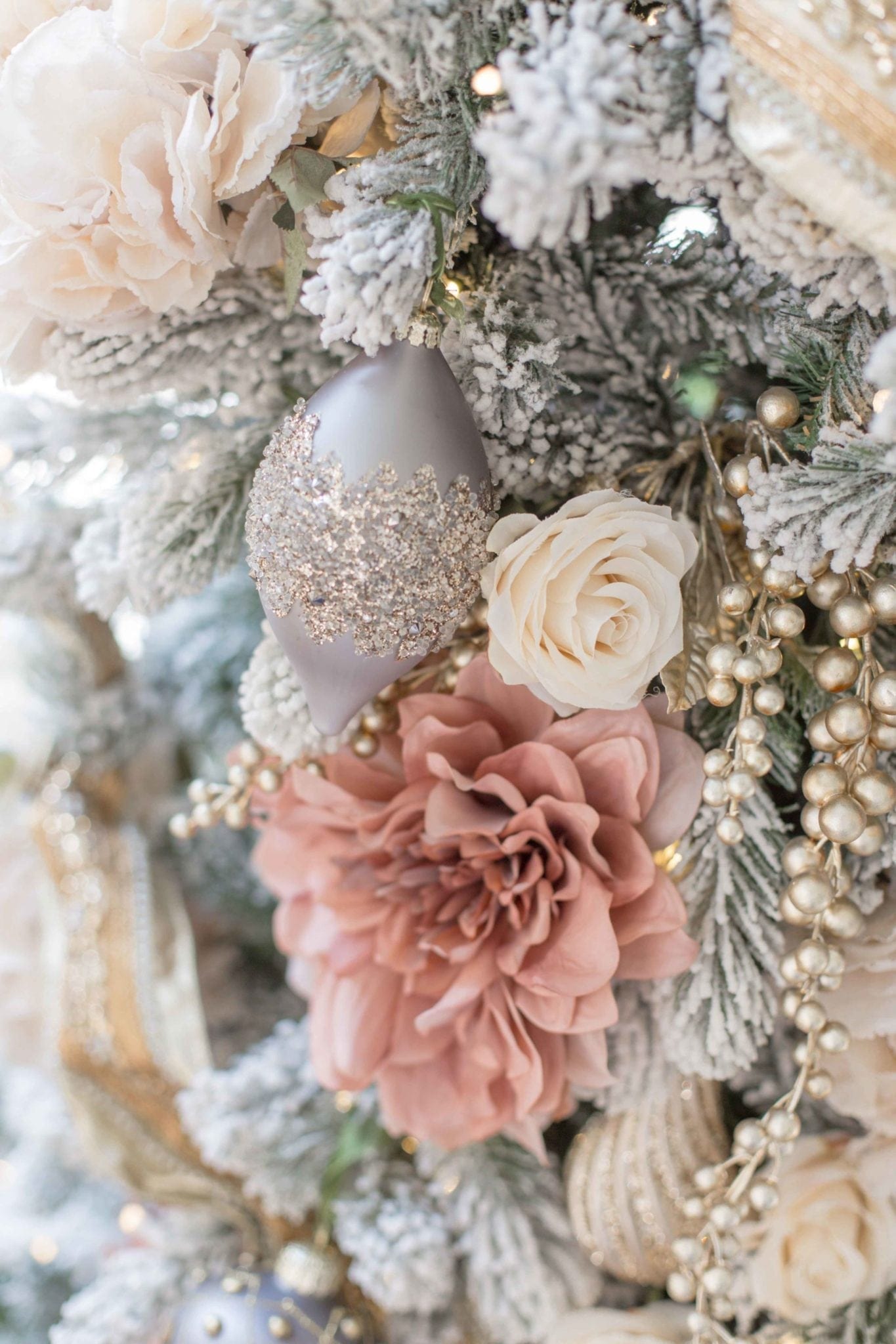 Artificial roses and gray ornaments add a pretty gray and pink design to this King of Christmas artificial tree. Tips to decorate a gray, pink, ivory and gold Christmas tree!
