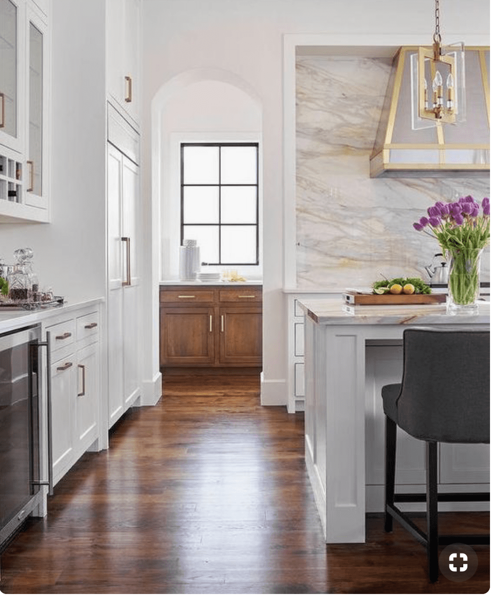Kitchen with marble backsplash and metal hood with warm wood floors.