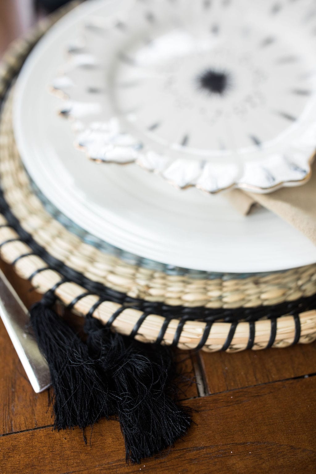Anthropologie charger plates. Chargers with black tassels on round rotten placemat.