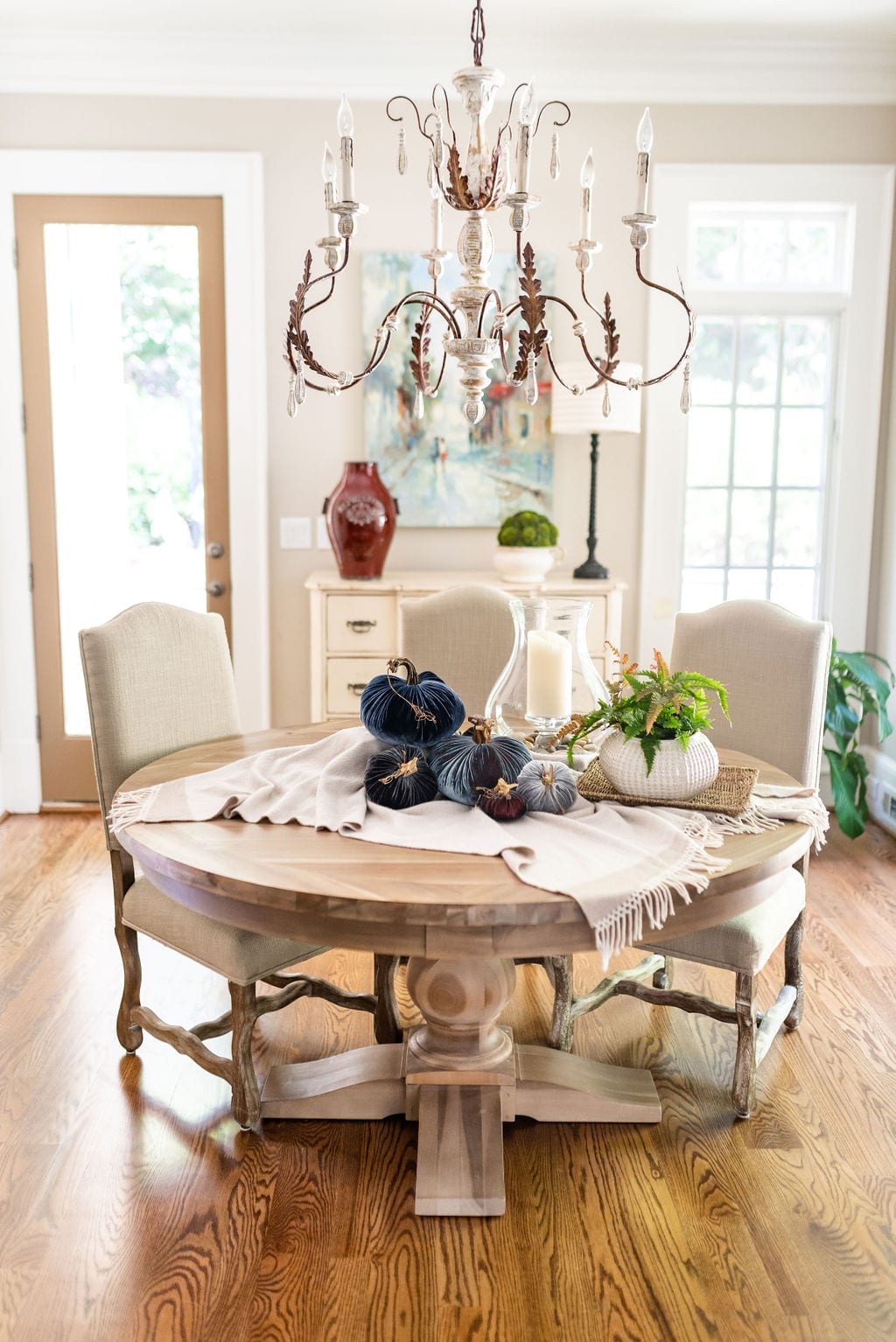 Thanksgiving Table set up with Plush Pumpkin. Rustic kitchen with chandelier and round wood dining room table.