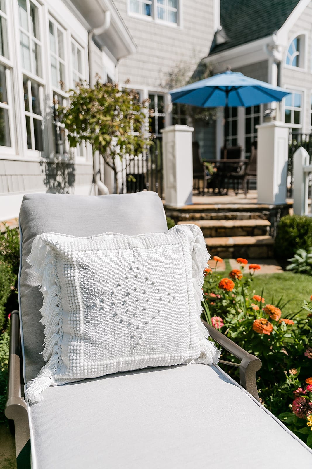 Serena and Lily White Outdoor Pillow on sale. Woodard Andover chaise lounge with Sunbrella blue outdoor umbrella.