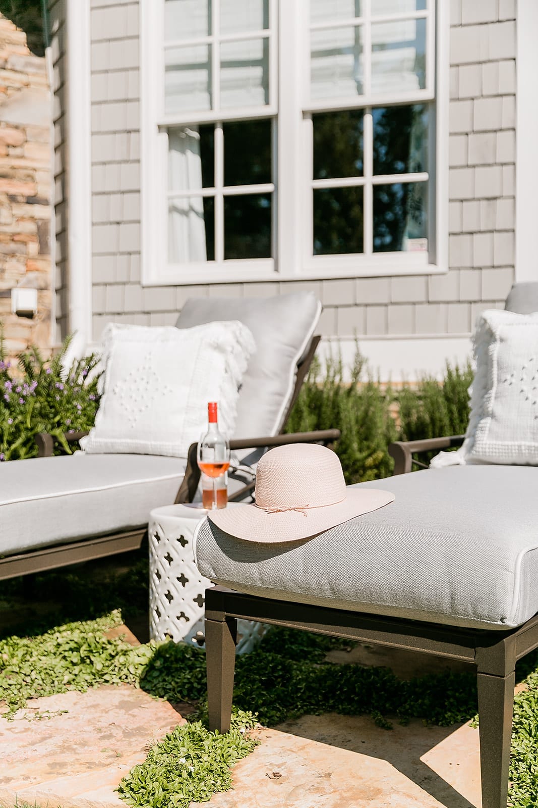 Comfy oversized chaise lounge chairs. Cedar house exterior Cape Cod style with gray outdoor furniture and white garden stool.
