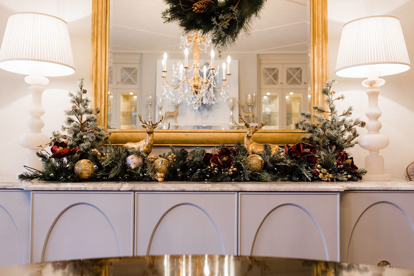 Need dining room christmas decorating ideas? Magnolia garland with lights. How to create a glamorous dining room setting for Christmas with gold reindeer and white table lamps.