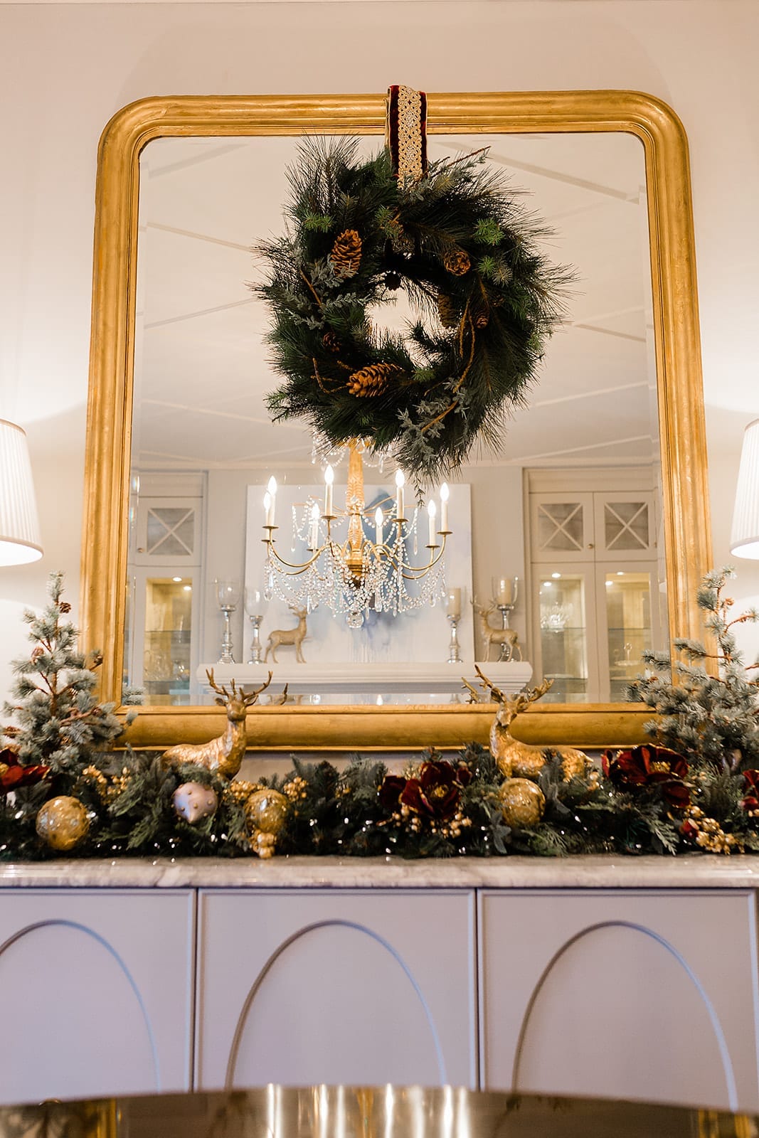 Grand dining room with gold chandelier and christmas wreath hung with Frontgate ribbon on mirror. Frontgate garland and holiday decor in dining room on tabletop with gold ornaments and holiday garland.