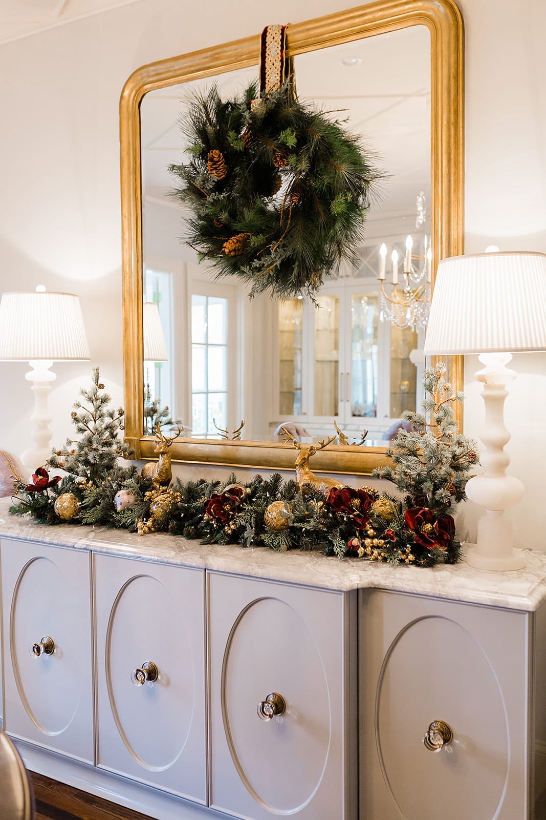 Christmas dining decor ideas. Gold ornate mirror with wreath hanging with Frontgate ribbon and white marble lamps.