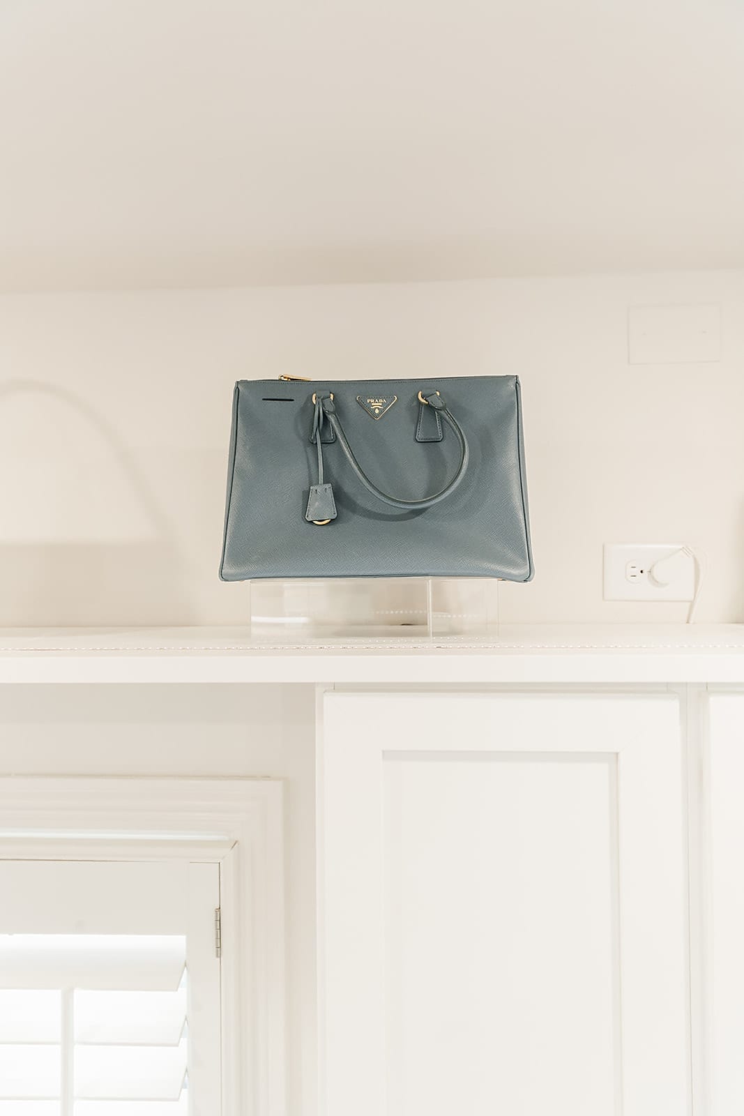 Blue Prada Purse on acrylic display stand in white closet.