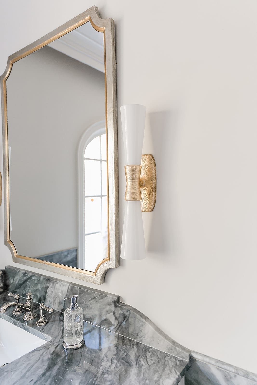 Kelly Wearstler Sconce in bathroom with gray marble and silver and gray mirror.