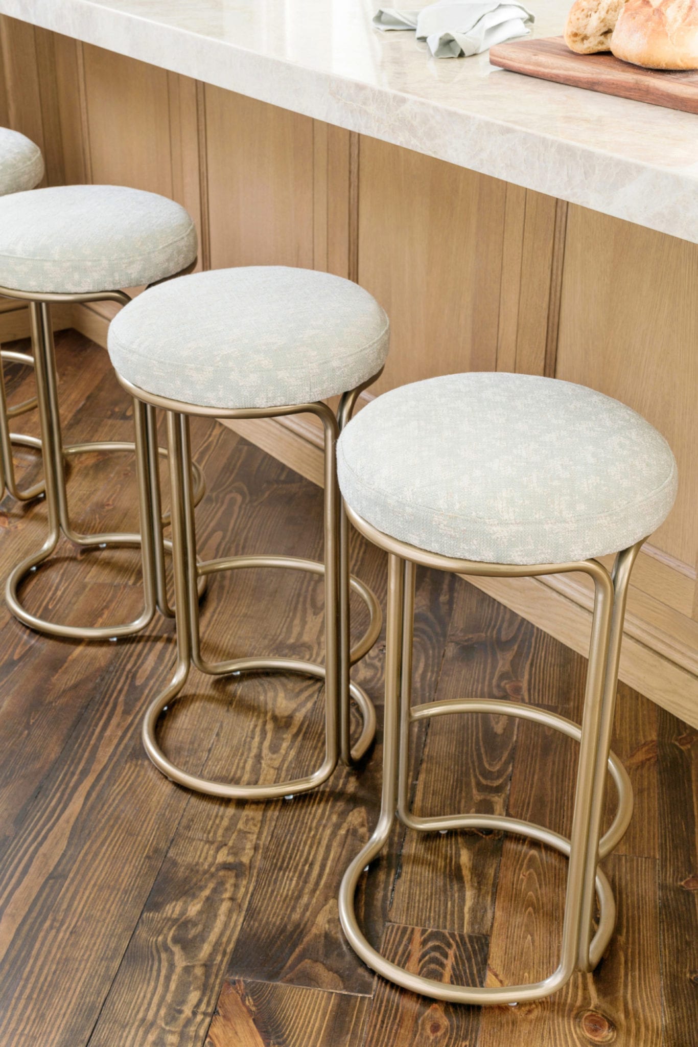 West Elm Counter Stools covered in Roma fabric with Taj Majal counter tops and stained wood kitchen floors.