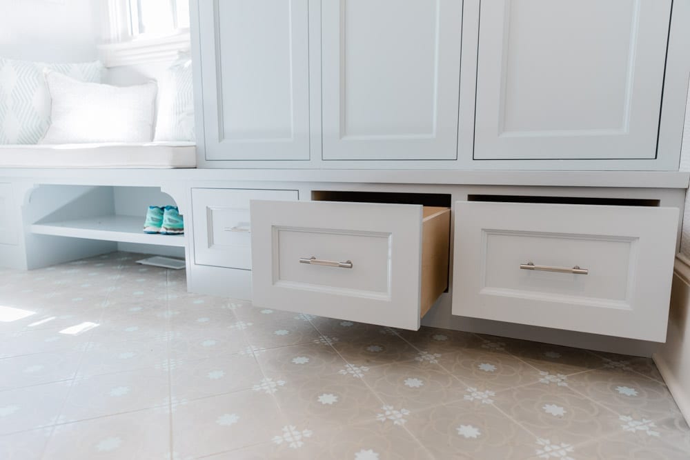 Mudroom organizing ideas. See our mudroom locker cubbies with doors, mudroom bench seat, roman shade and throw pillows all decorated with blue cabinetry, silver lantern pendant and patterned clement tile floor.