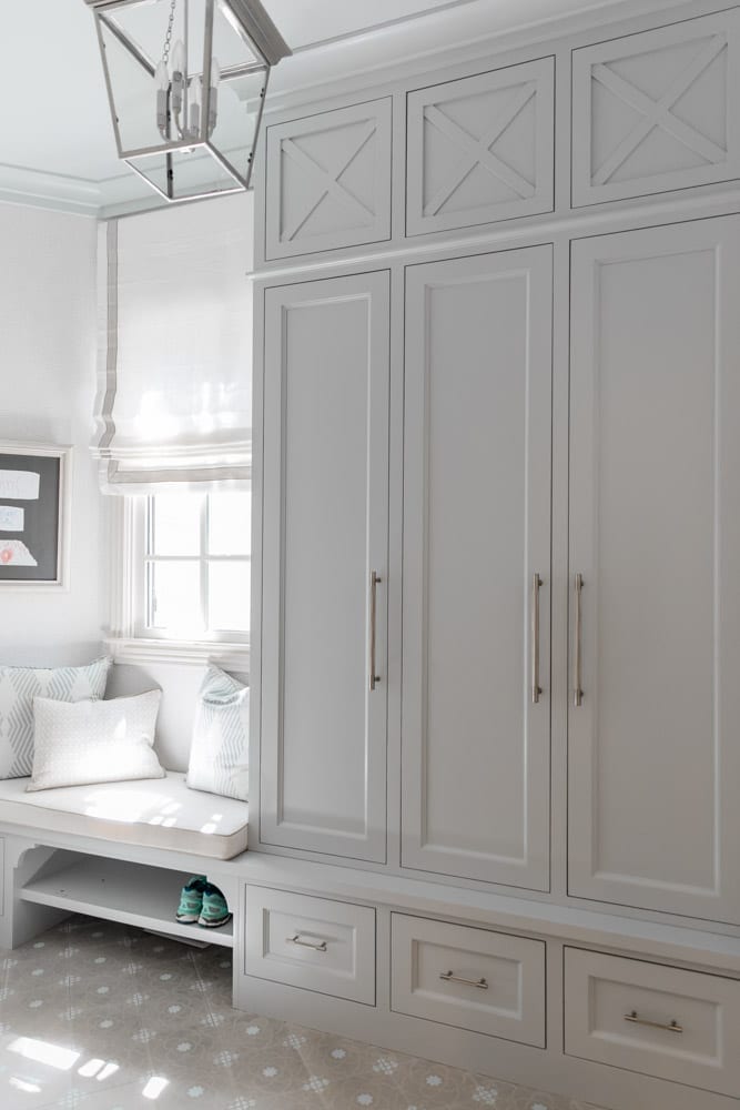 Mudroom organizing ideas. See our mudroom locker cubbies with doors, mudroom bench seat, roman shade and throw pillows all decorated with blue cabinetry, silver lantern pendant and patterned clement tile floor.