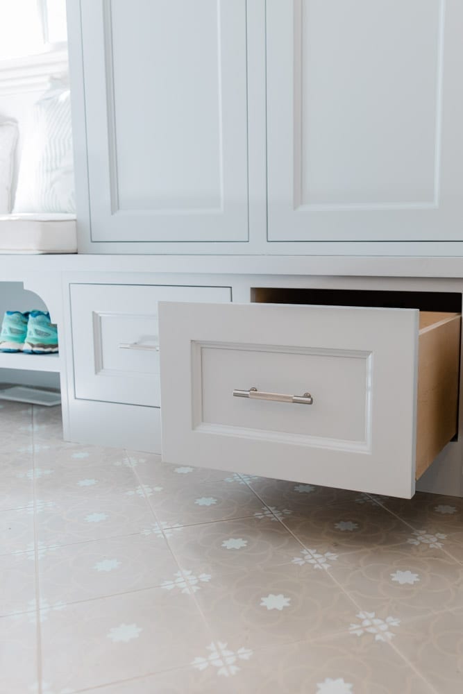 Mudroom organizing ideas. See our mudroom locker cubbies with doors, mudroom bench seat, roman shade and throw pillows all decorated with blue cabinetry, silver lantern pendant and patterned clement tile floor.
