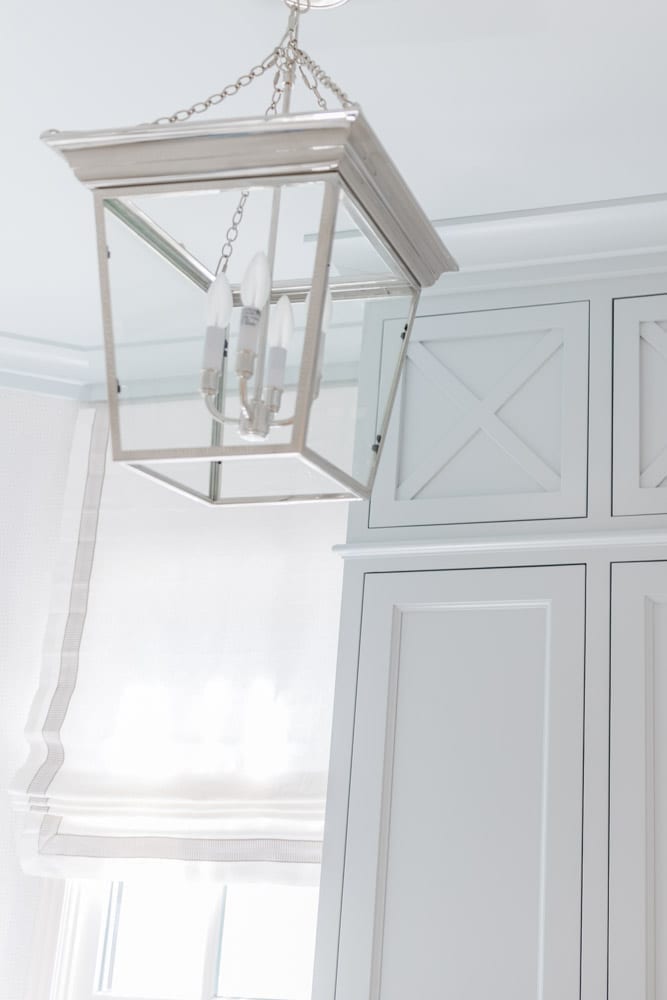 Mudroom organizing ideas. See our mudroom locker cubbies with doors, mudroom bench seat, roman shade and throw pillows all decorated with blue cabinetry, silver lantern pendant and patterned clement tile floor.