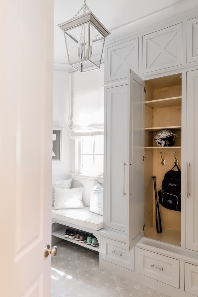 Mudroom organizing ideas. See our mudroom locker cubbies with doors, mudroom bench seat, roman shade and throw pillows all decorated with blue cabinetry, silver lantern pendant and patterned clement tile floor.