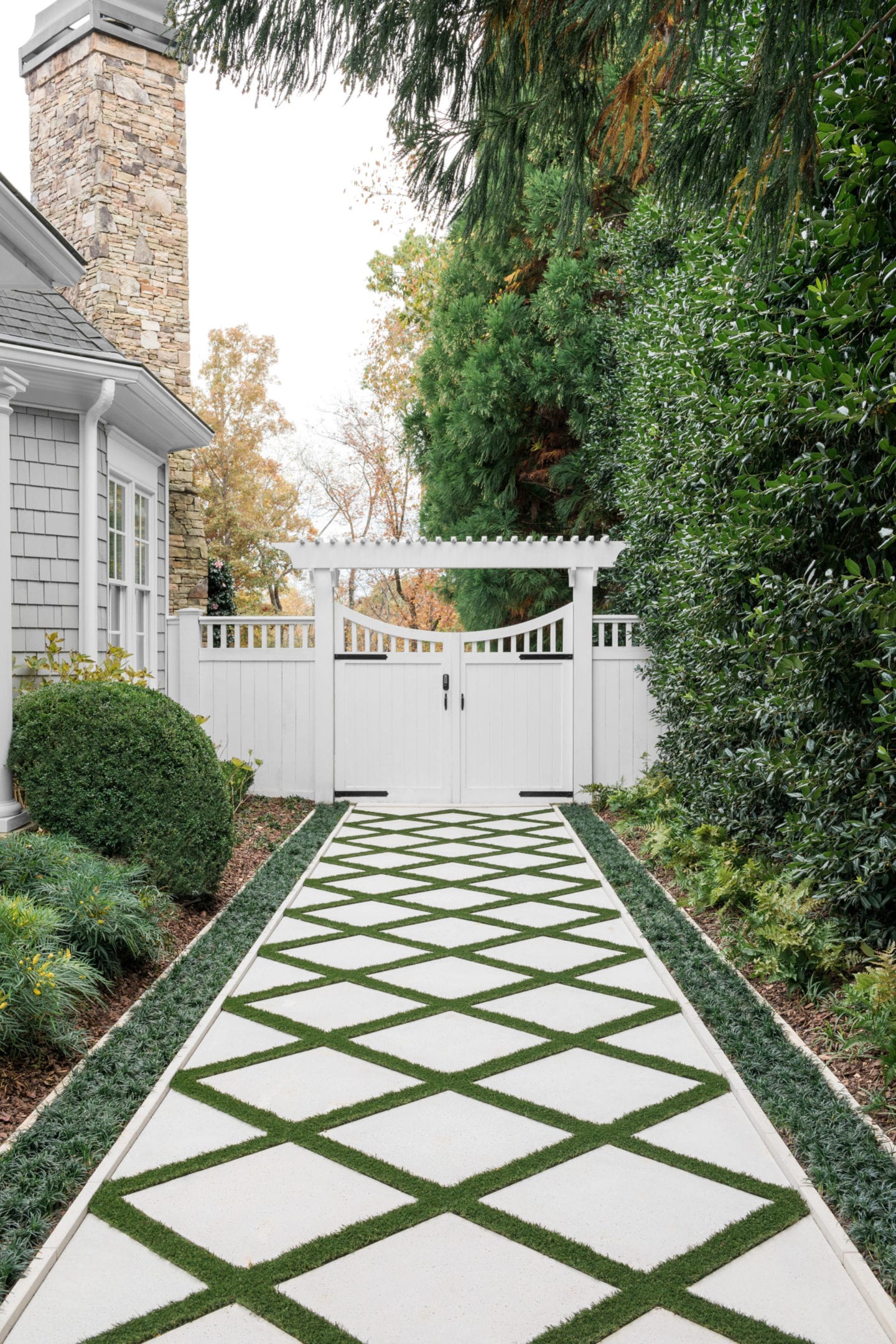Water drainage is fixed showing a limestone exeterior walkway path crosshatched and landscaped with astro turf. The path leads to a white cedar fence and past a home with cedar siding painted in SW Dorian Gray.