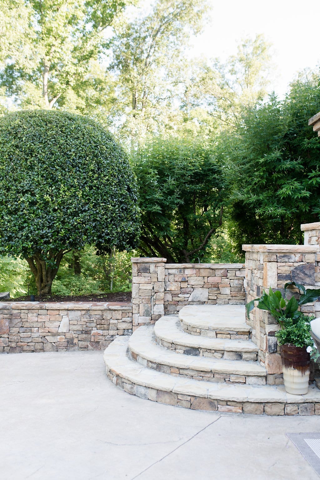 Concrete and stone stairs lead up from a pool deck area surrounded by two Vitex trees and one shaped Holly tree.