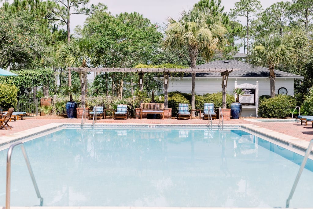 A cool pool deck for pools is done with brick making it both gather water and feel cool to your feet. This Florida pool design also features a wood arbor to help with shade on the teak outdoor furniture.