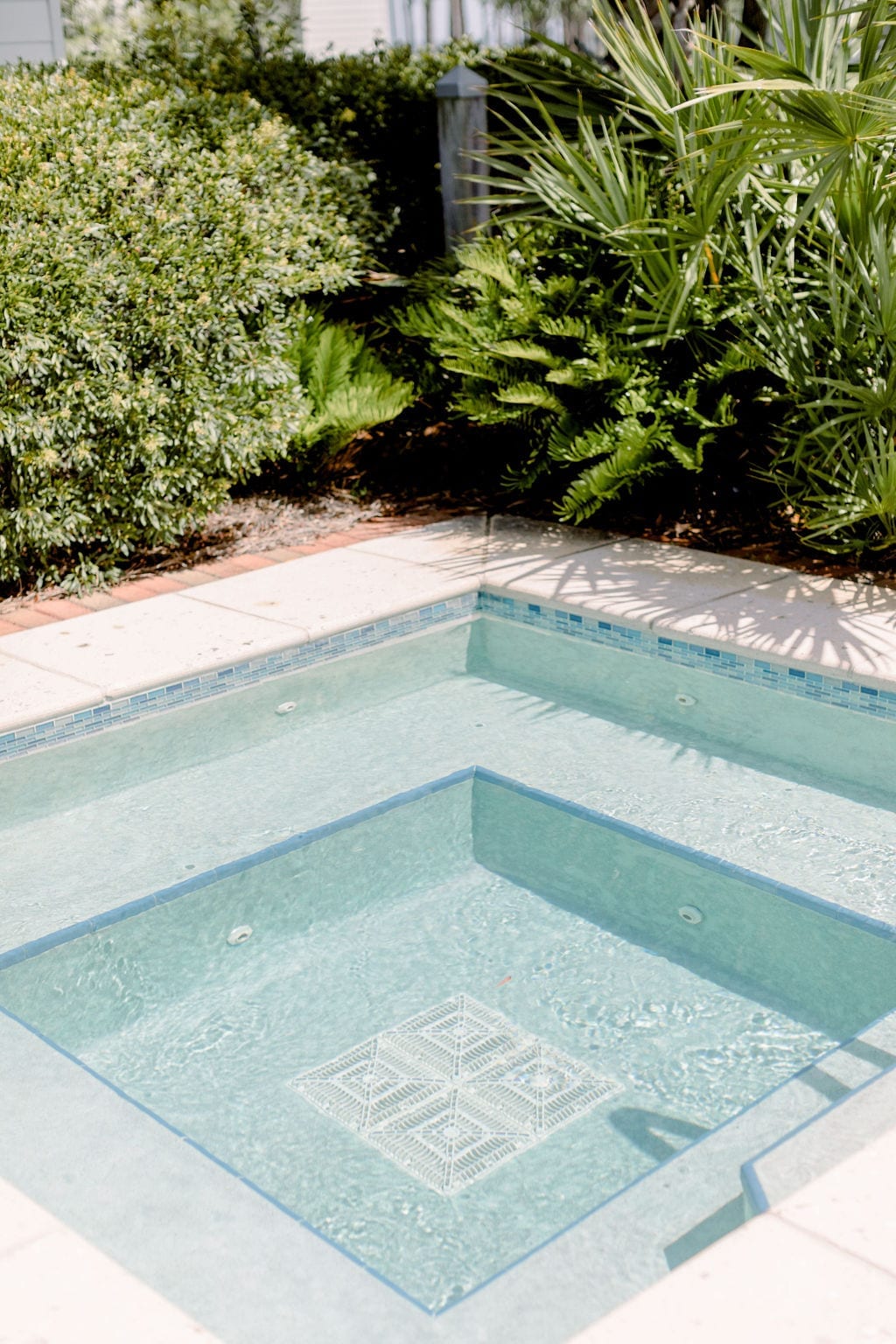 An inground Florida pool has a square hot tub framed with light blue modern pool tiles.