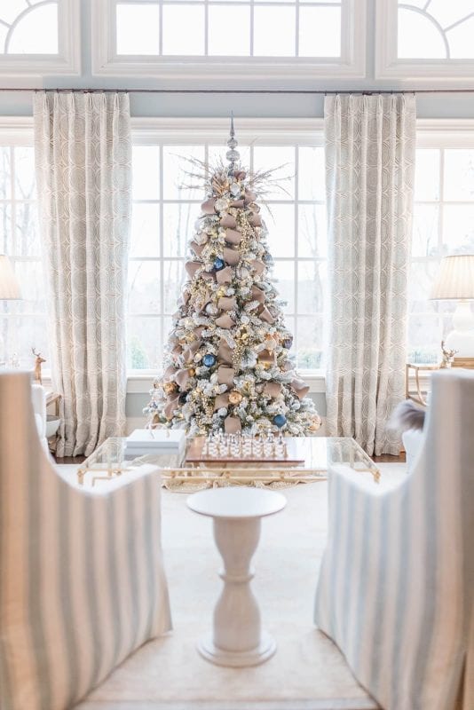 A Taupe velvet ribbon Christmas tree with blue ornaments from Frontgate collection and Frontgate tree topper. A gold Christmas skirt finishes off the taupe and navy blue accented flocked Christmas tree.