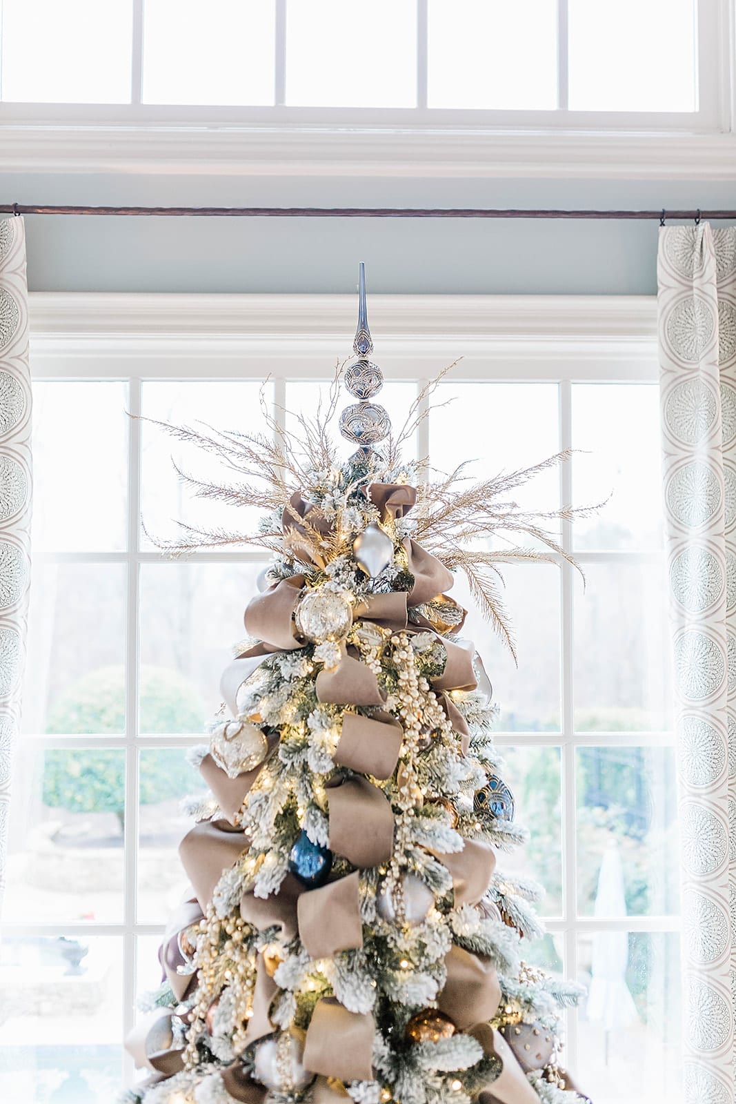 A Taupe velvet ribbon Christmas tree with blue ornaments from Frontgate collection and Frontgate tree topper. A gold Christmas skirt finishes off the taupe and navy blue accented flocked Christmas tree.