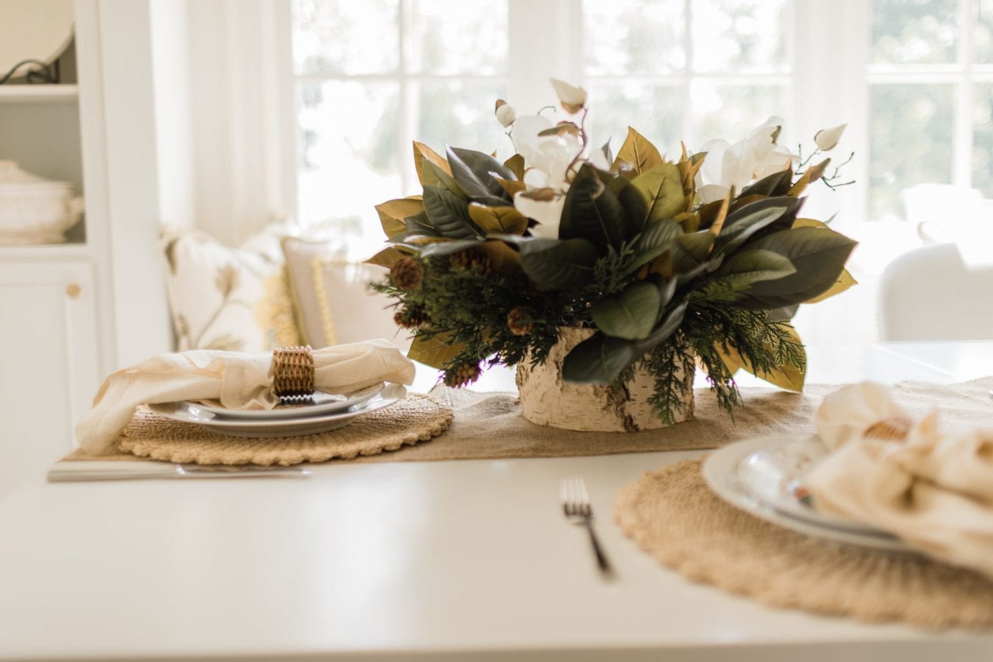 Faux Fall Flower Arrangement on a white table with wicker and rattan and birch accessories for a super easy, affordable and long lasting autumn table. Magnolia centerpiece with white flowers and faux mangolia leaves.