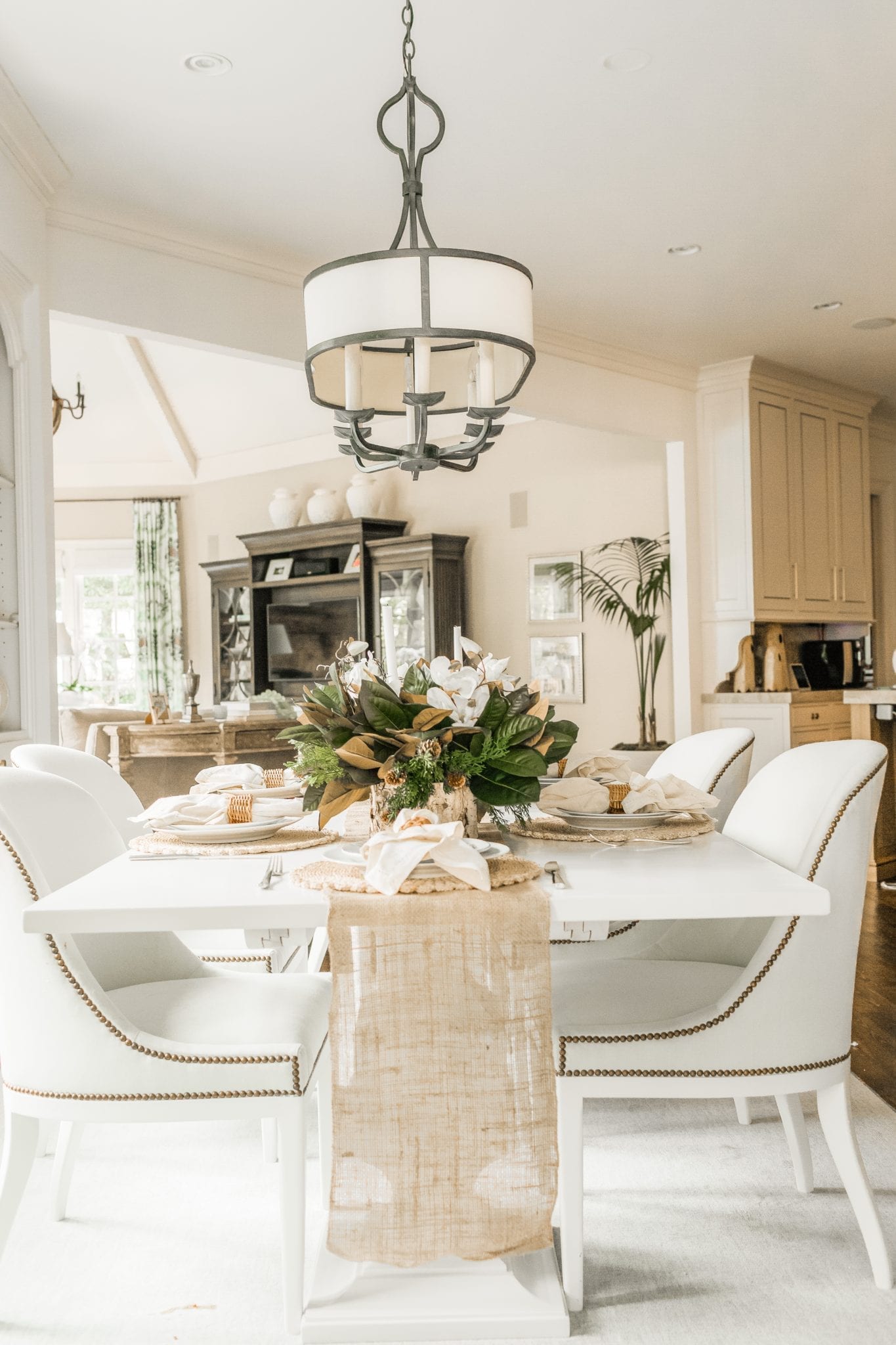 White dining room table set with a burlap table runner, wicker kitchen accessories (can be replaced with round rattan placemats) and birch and magnolia table settings. Example of white table decor.