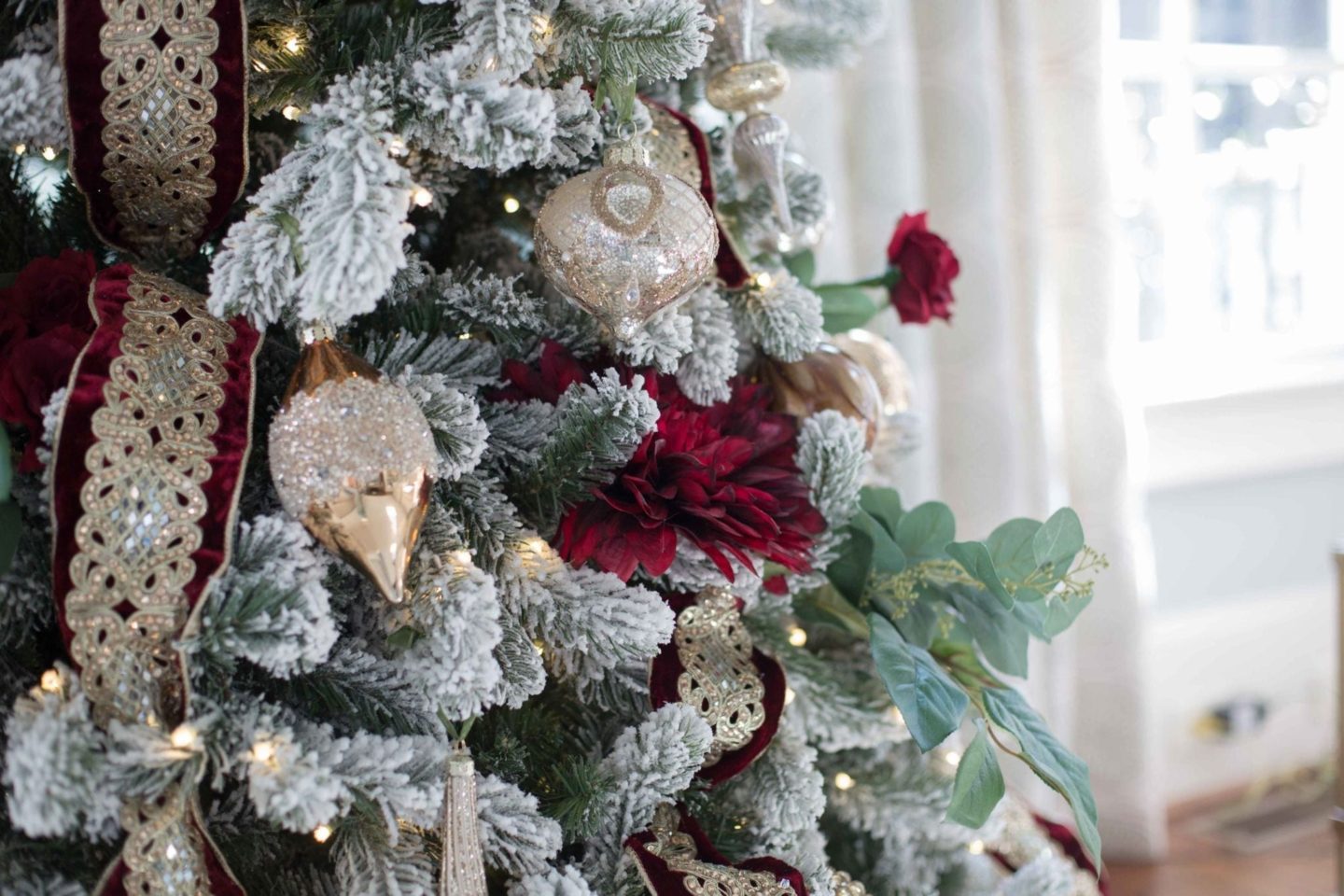 Red and green and gold white flocked christmas tree with Frontgate ornaments and silk red flowers.