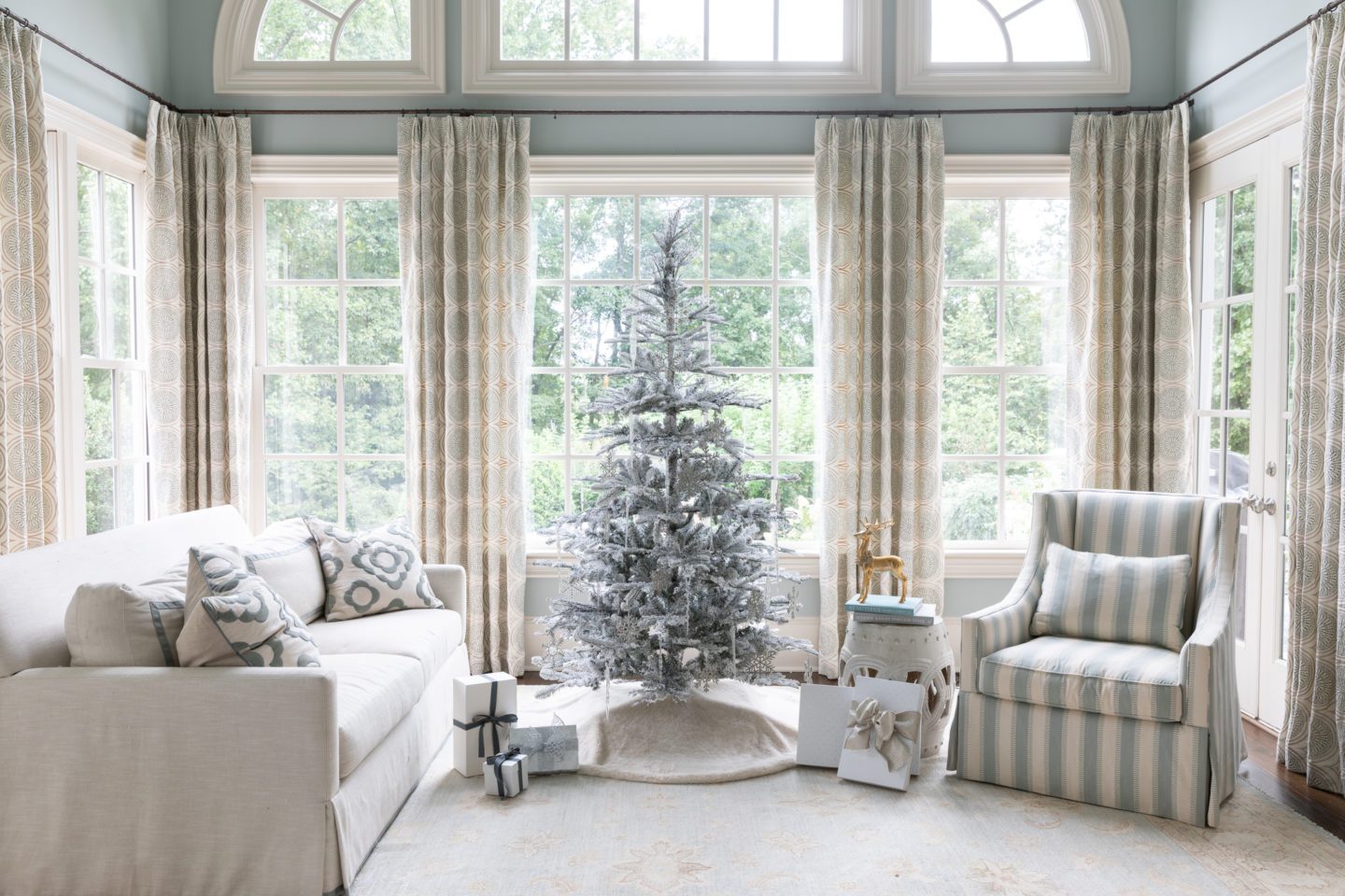 Flocked Christmas Tree in front of a large window with silver and white ornaments.