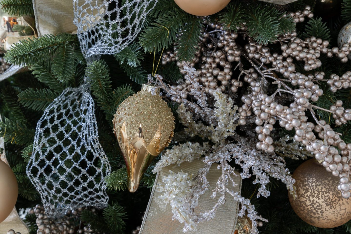 Gold ornaments with gold picks and mesh ribbon on a green Christmas tree.