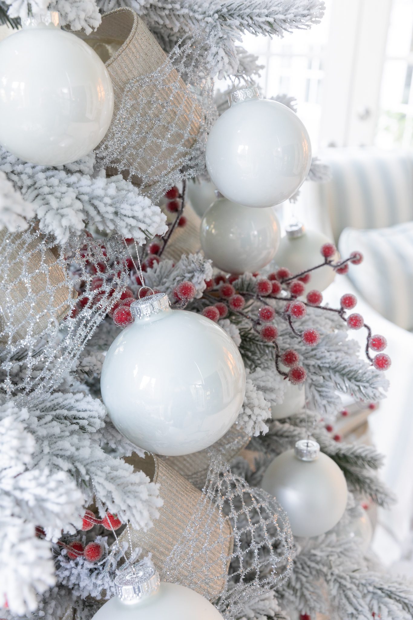 A flocked tree with red berry pick decor and white ornaments and ribbon.