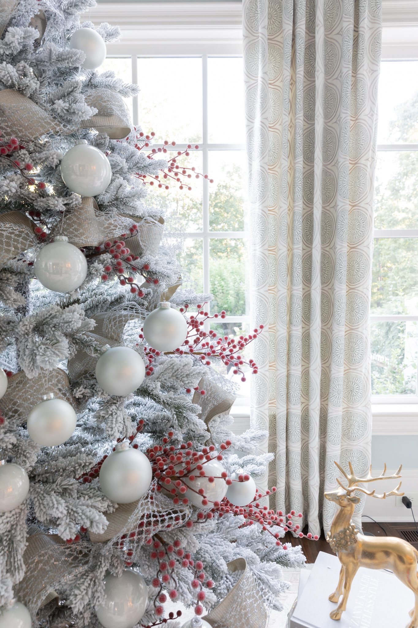 White ornamnets with red holly berries hanging on a flocked Christmas tree